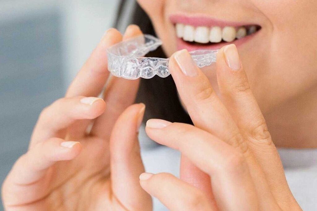 Person holding clear Invisalign aligners for teeth straightening with a natural smile.